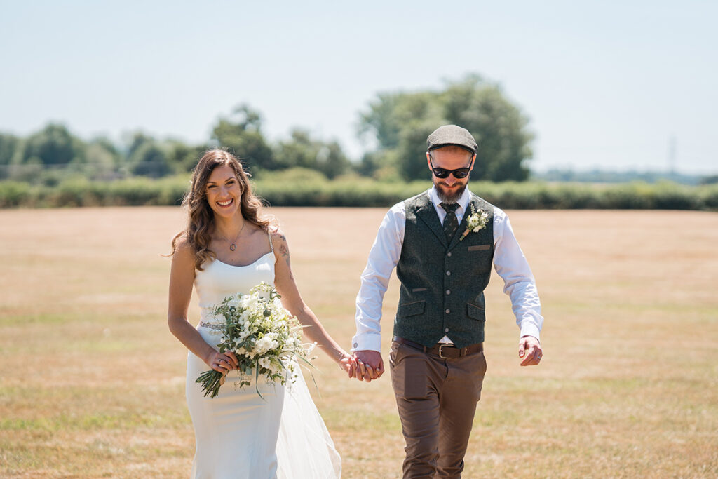 bride and groom walk hand-in-hand across a field at their new forest wedding