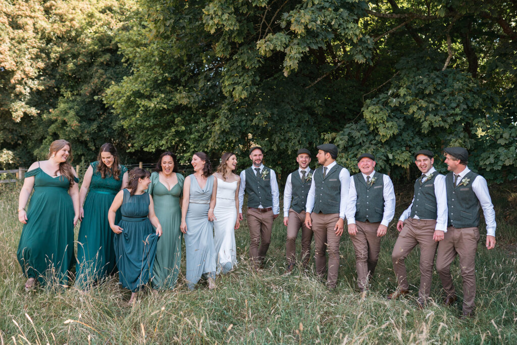 bride and groom with their bridal party all wearing green tones in the woodland