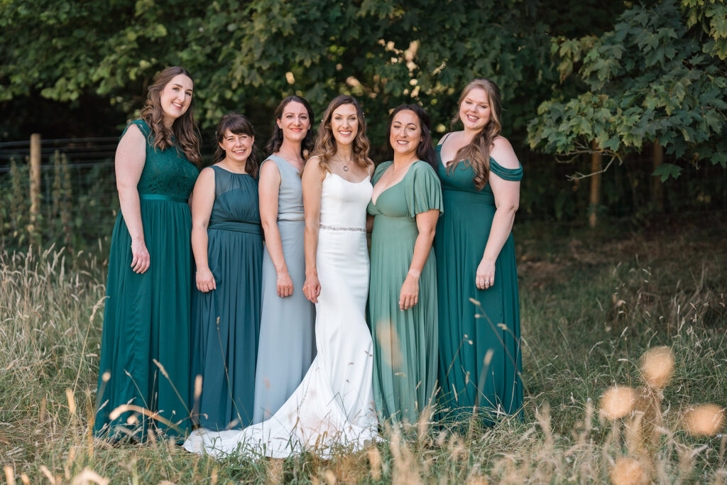 bride and groom with their bridal party all wearing green tones in the woodland