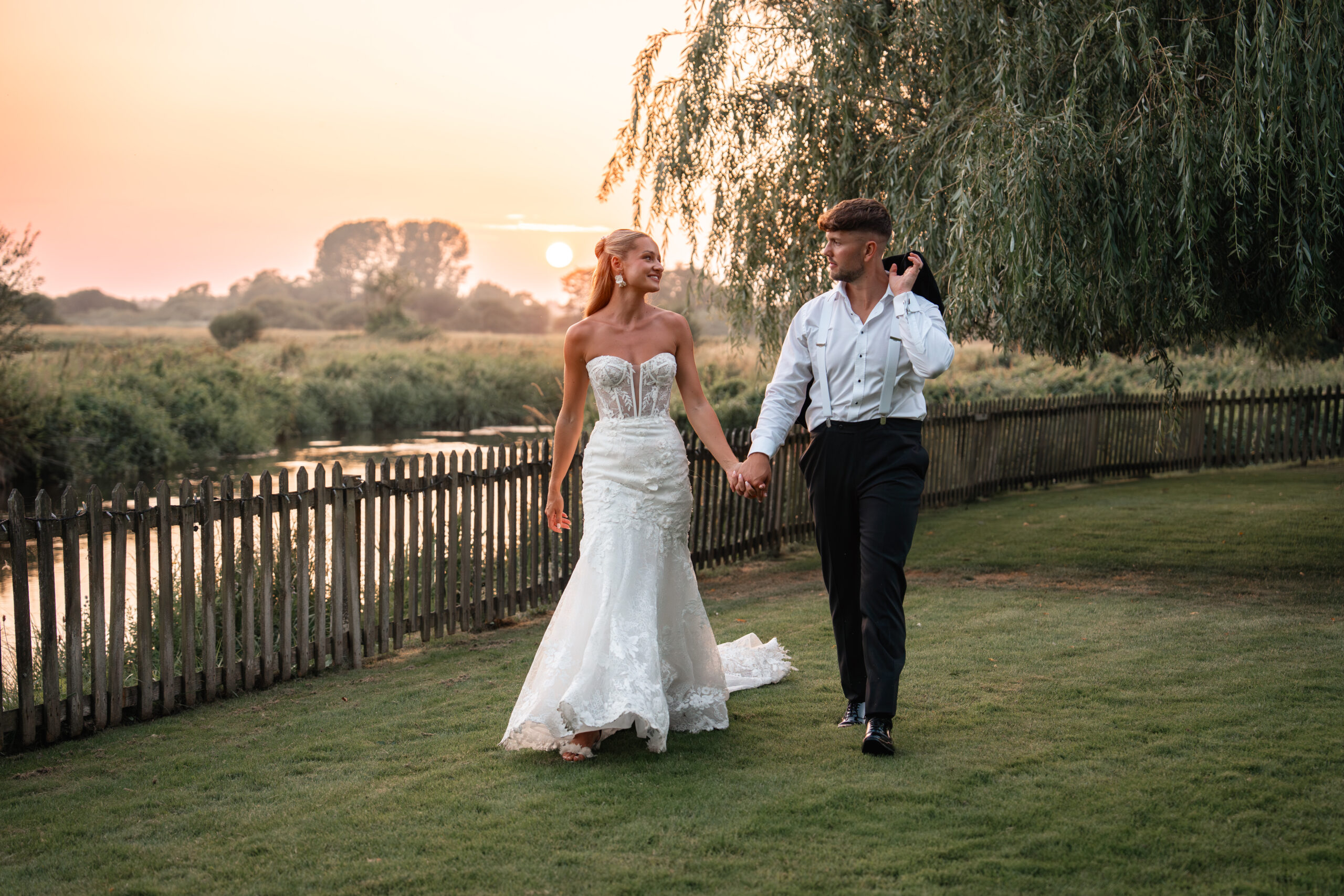 Bride and groom walk hand-in-hand on the grass at sunset at Sopley Mill Wedding