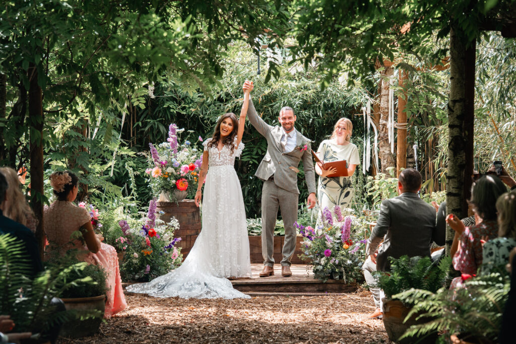 Bride and Groom hold hands in the air at Harewood Forest after becoming husband and wife 