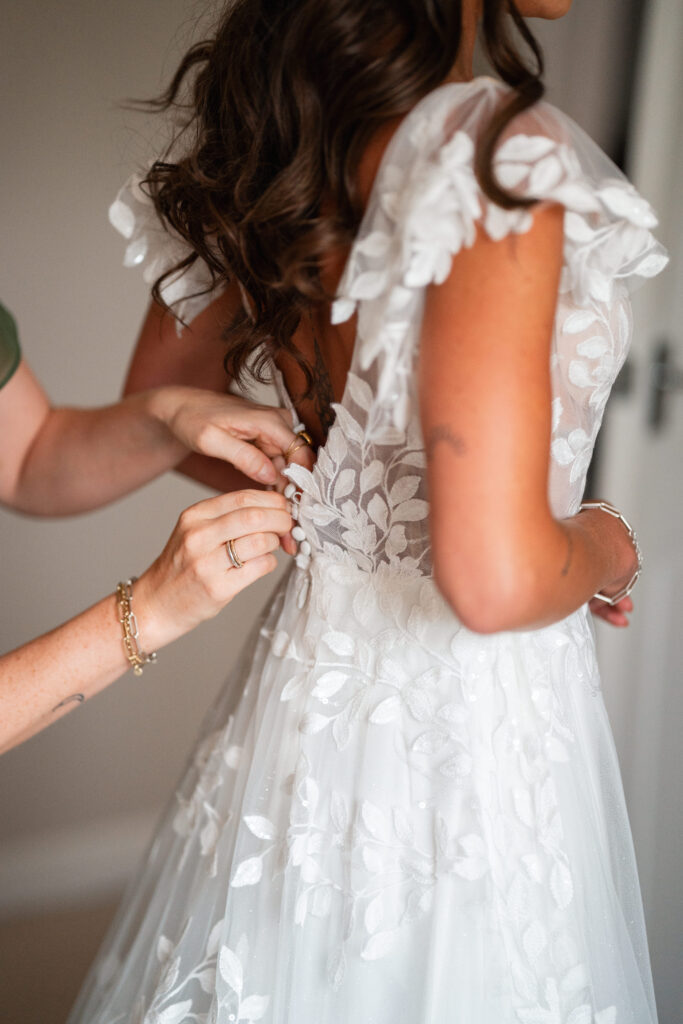 sister does up brides floral dress on wedding day 