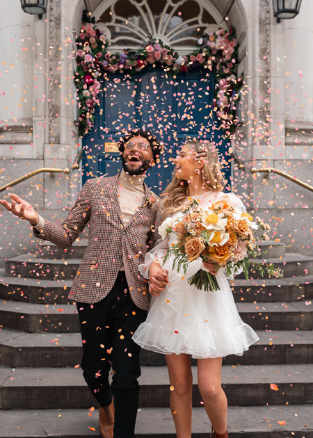bride and groom laugh as confetti falls on steps at chelsea town hall wedding