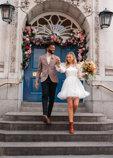 newly wed couple walk down steps at Chelsea Old Town Hall, bride wears short white dress