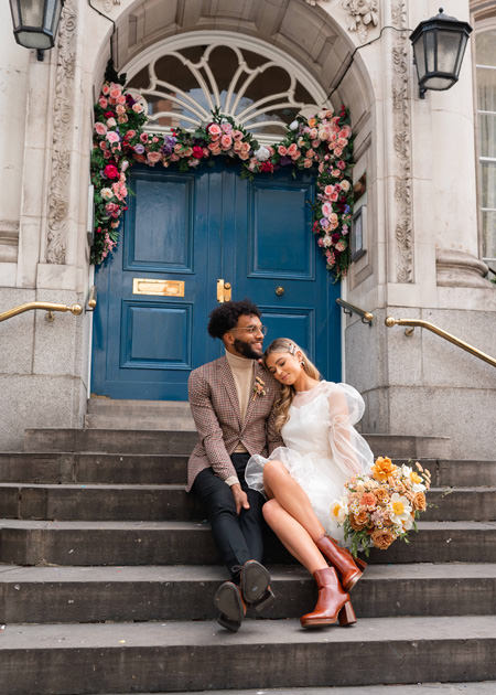 bride rests head on grooms shoulder as they sit on steps at Chelsea Town Hall