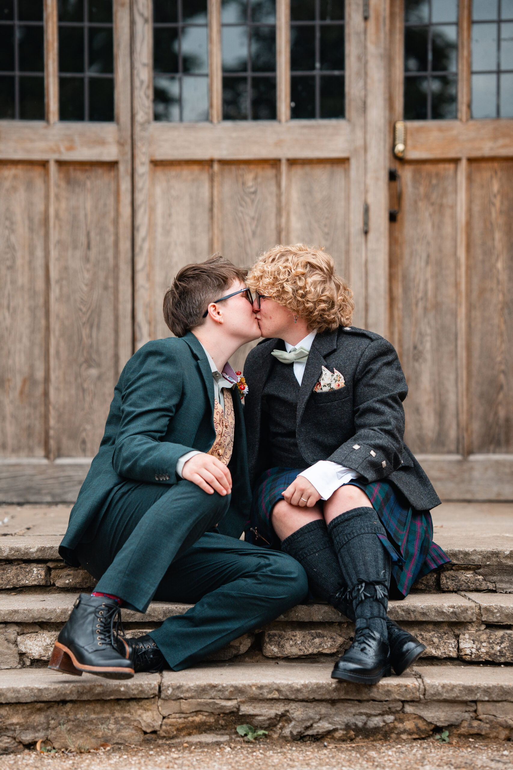 non-binary couple sit on steps sharing first kiss at wedding