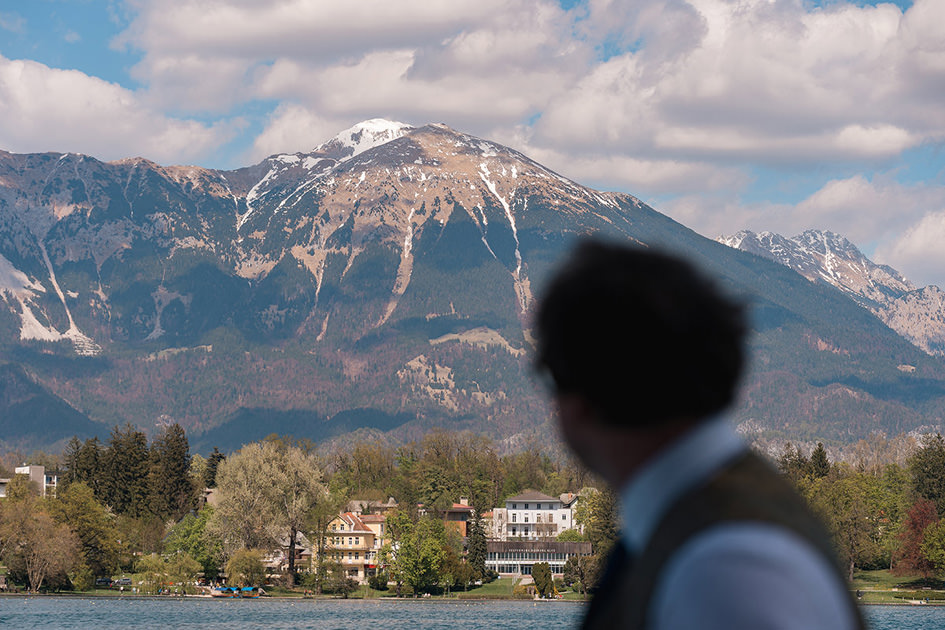 Groom looks out at mountains over Lake Bled