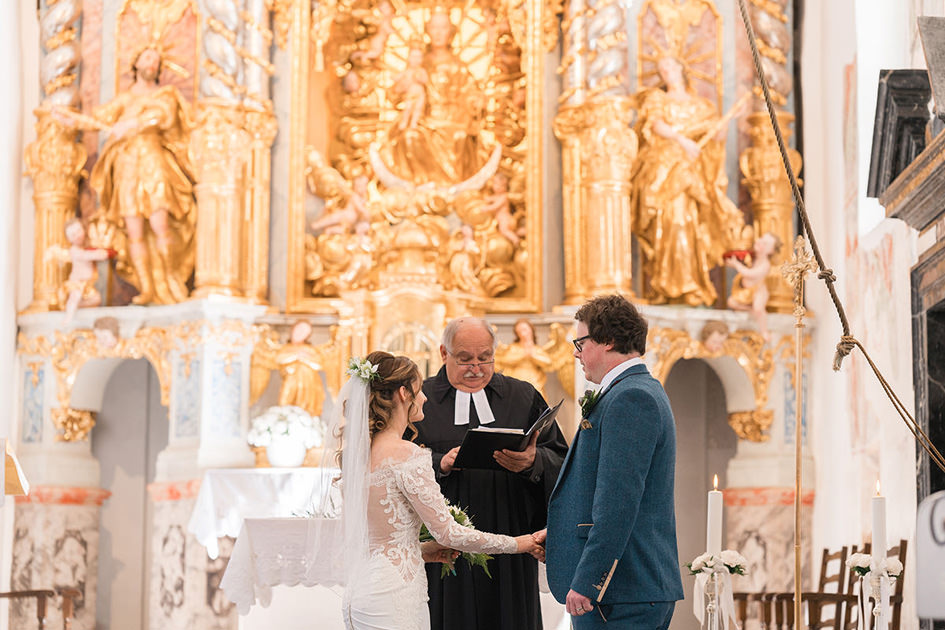 Bride and Groom stand in front of golden altar inside church